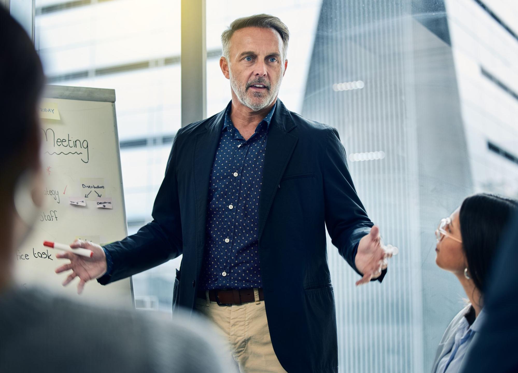 group at a desk and man leading teaching on a whiteboard